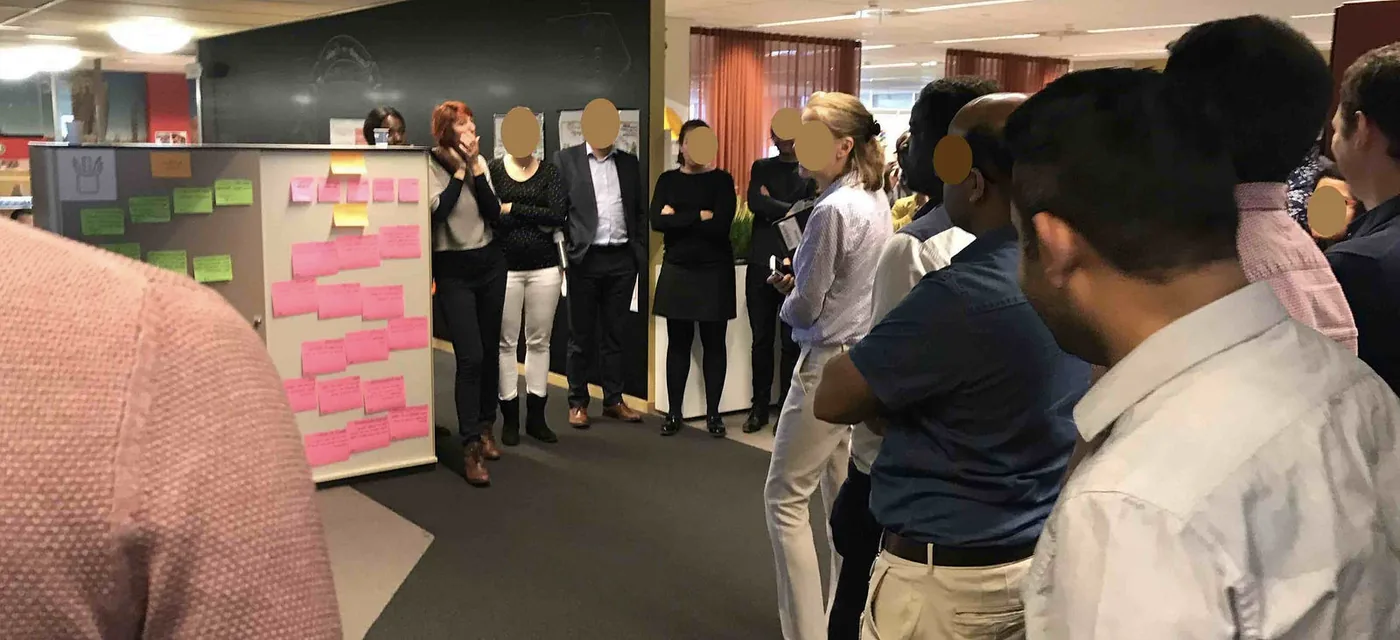 Participants standing around a wall of pink sticky notes at the start of the overall multi-team refinement session