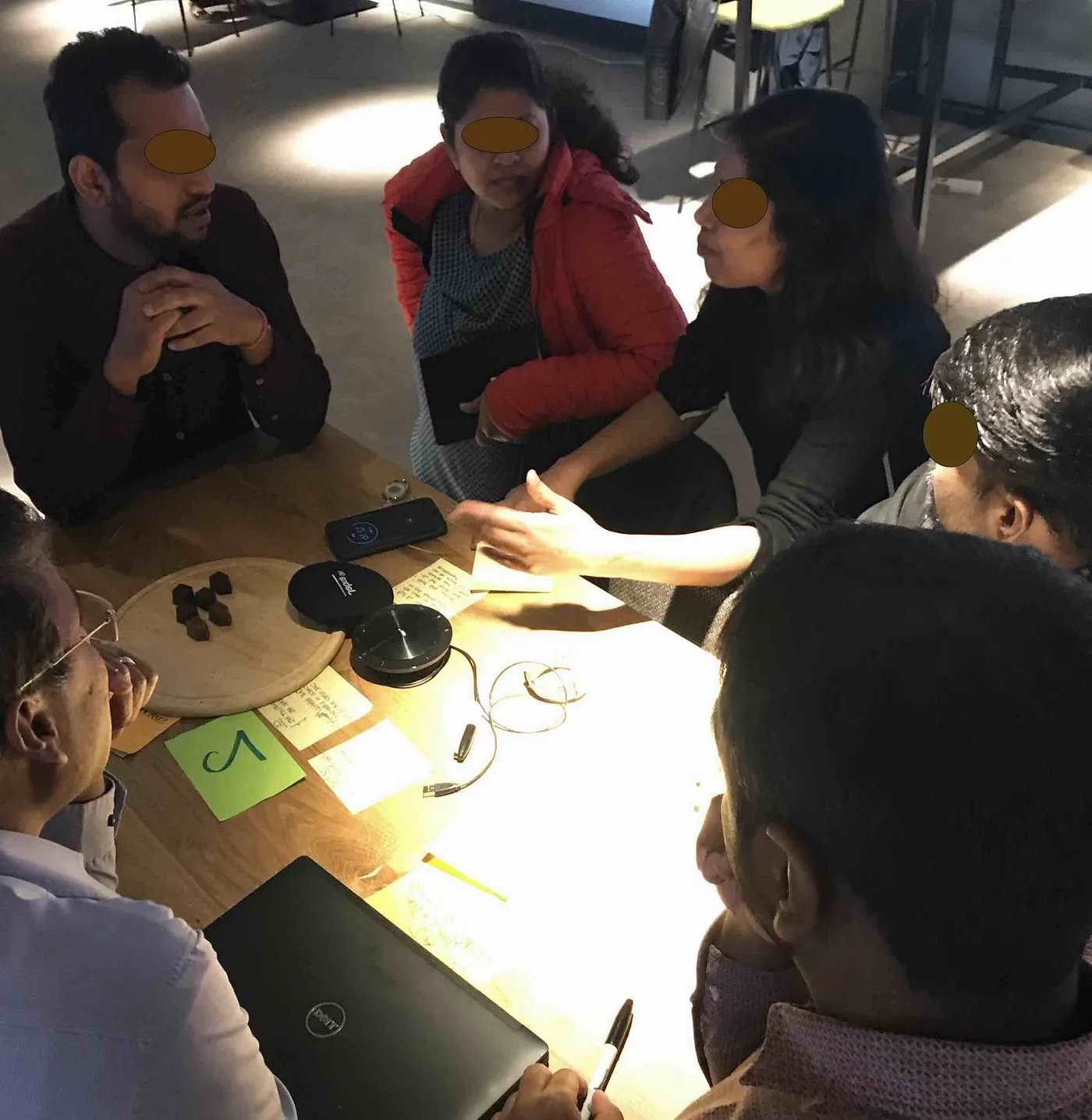 Small group at a numbered station table discussing a backlog item, with sticky notes and a laptop