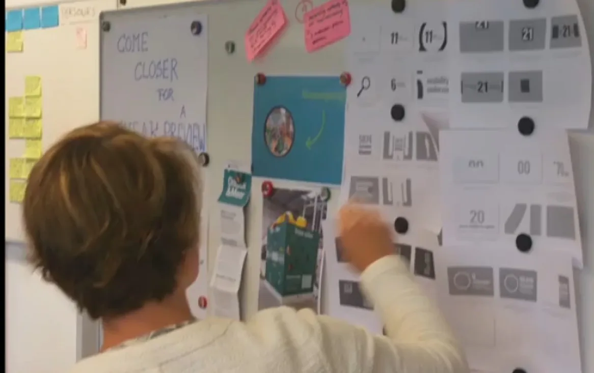 Visitor browsing a team's feature shop board titled Come closer for a sneak preview, during a Sprint Review round