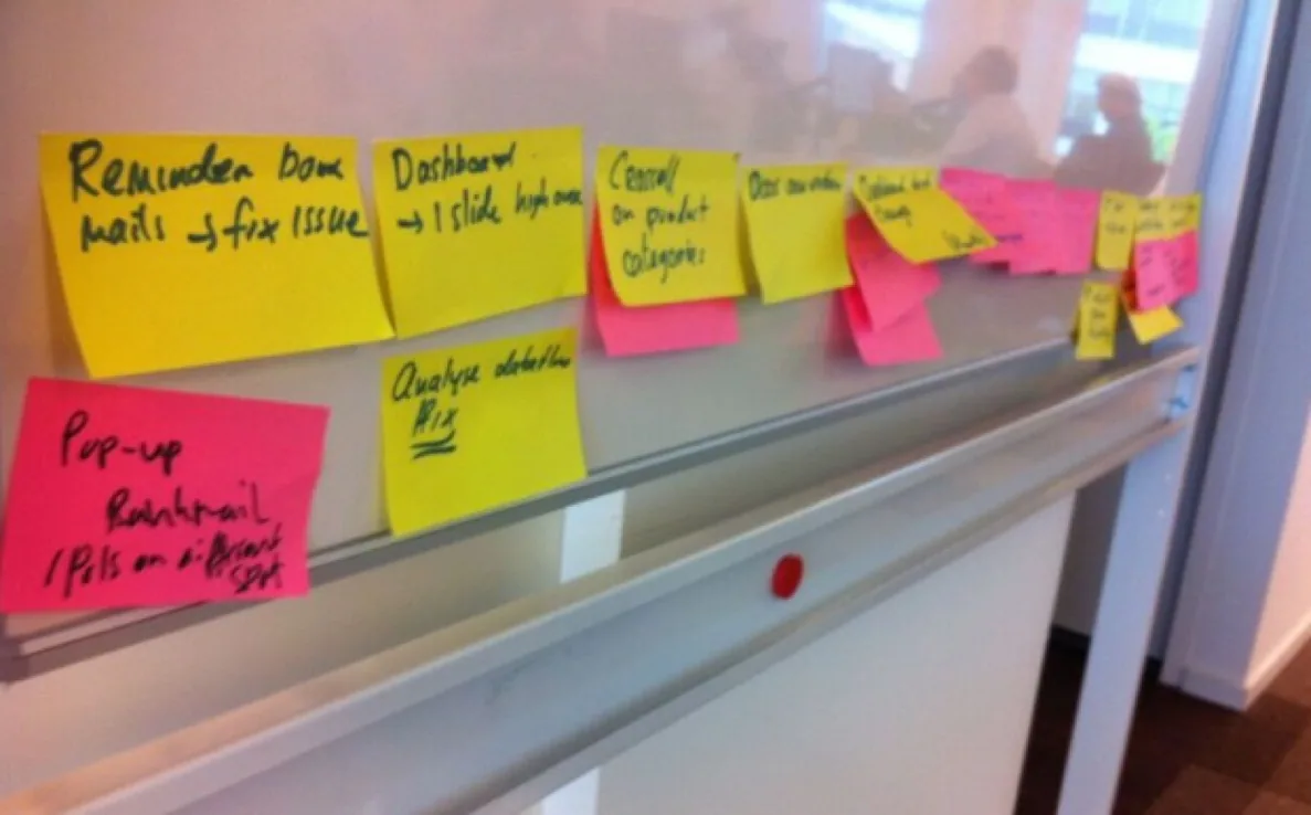 Sticky notes with stakeholder feedback lined up on a whiteboard ledge, grouped by feature for the Product Owner